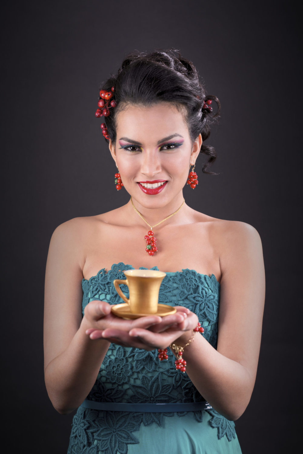 Donna elegante in abito verde petrolio che sorregge una tazzina da caffè dorata, servizio fotografico Nerino Caffè.